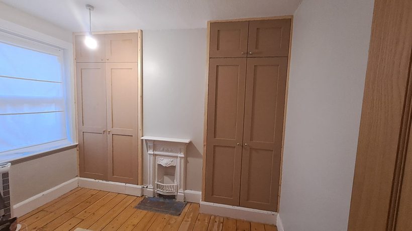 A wide lit media wall with TV, shelving and base cupboards in warm pine and grey