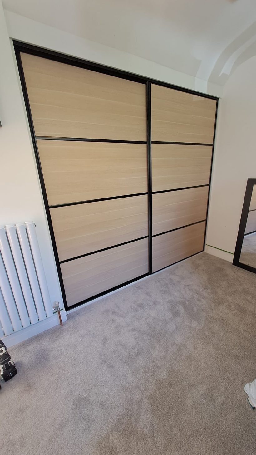 Fitted sliding wardrobe with oak veneer panels and black aluminium frame